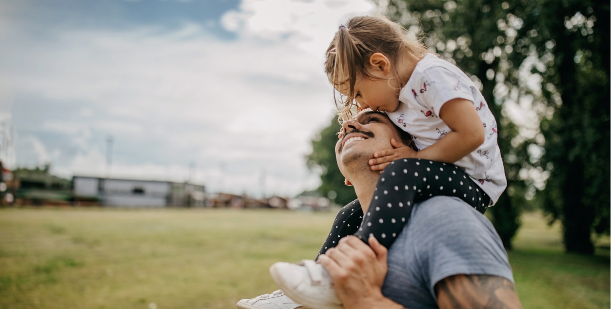 smiling dad with his daughter on his shoulders while they are in a field