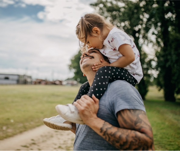 smiling dad with his daughter on his shoulders while they are in a field